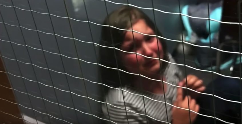 Zdjęcie przedstawia zapłakaną dziewczynkę, siedzącą w zakratowanym pomieszczeniu