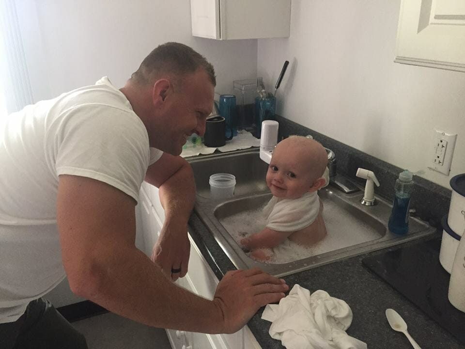 mężczyzna kąpie dziecko w zlewozmywaku