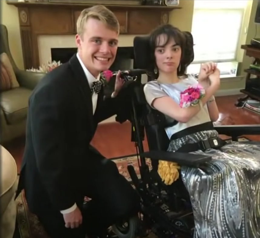 chłopak w garniturze kuca obok dziewczyny w sukience siedzącej na wózku inwalidzkim