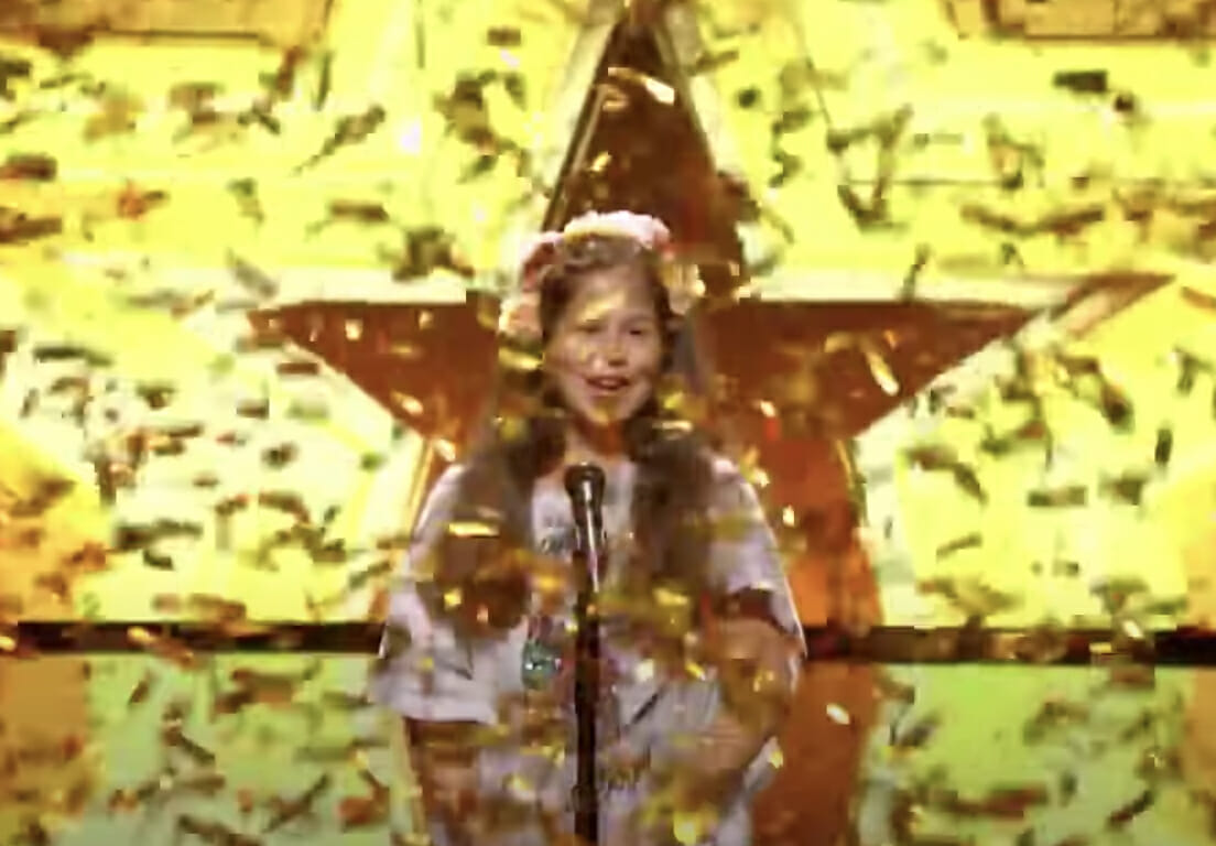 dziewczynka stoi przy mikrofonie i dookoła spada złote konfetti 