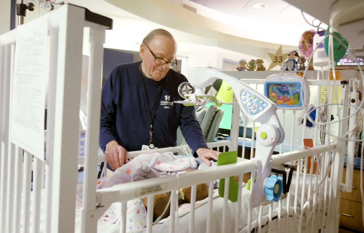 starszy mężczyzna w okularach stoi przy dziecięcym, szpitalnym łóżku