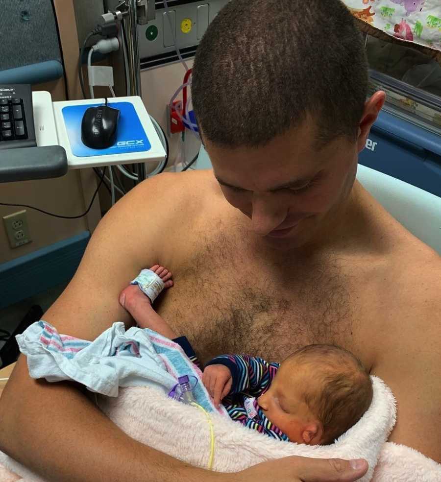 mężczyzna trzyma noworodka na klatce piersiowej